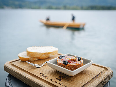 Foto Simeon Baker: Ein Tatar mit Brot bei der mundART Roas in St. Wolfgang. Im Hintegrund sieht man ein Traunerl auf dem Wolfgangsee.